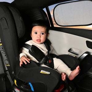 Child in a car seat inside a vehicle with a desert landscape visible through the window.