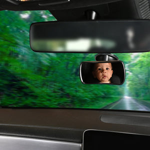 Car interior with a baby in a rearview mirror and a wider view of the road ahead.