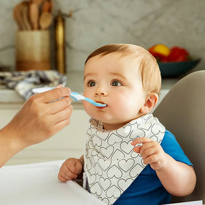 Baby being fed with a spoon by an adult in a kitchen setting
